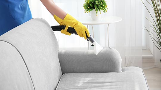 woman wear uniform cleaning upholstery with vacuum cleaner